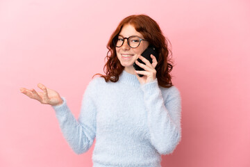 Teenager reddish woman isolated on pink background keeping a conversation with the mobile phone with someone