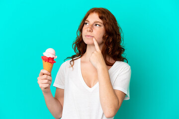 Teenager reddish woman with a cornet ice cream isolated on blue background having doubts while...