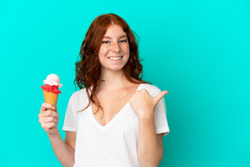 Teenager reddish woman with a cornet ice cream isolated on blue background pointing to the side to present a product