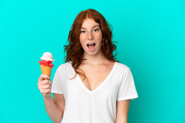 Teenager reddish woman with a cornet ice cream isolated on blue background with surprise facial expression