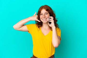 Teenager reddish woman using mobile phone isolated on blue background making phone gesture. Call me back sign