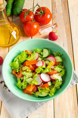 Recipe for vegetable salad with tomatoes, cucumbers and radishes. Seasonal dish on wooden background. Vegan food for diet.