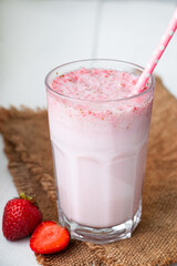 Cold milkshake with strawberries on white background. Summer drink in a glass with a paper straw.