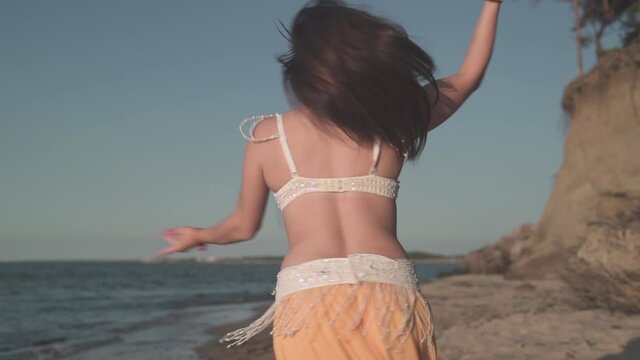 A beautiful girl in an oriental yellow dress dancing a belly dance on the coast of the sea. 50fps