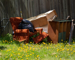 Old furniture and garbage sitting outside in a dandelion field