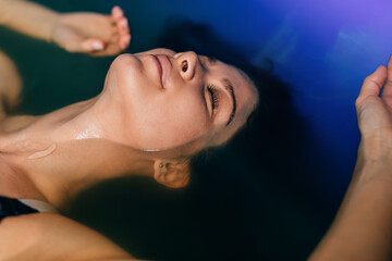 Beautiful woman floating in tank filled with dense salt water used in meditation, therapy, and alternative medicine. .
