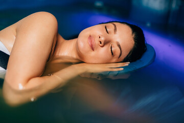 Beautiful woman floating in tank filled with dense salt water used in meditation, therapy, and...