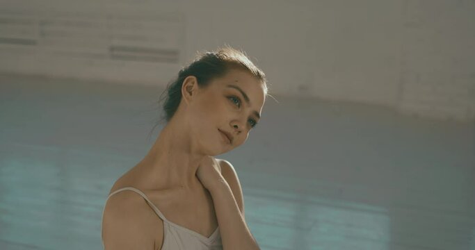 Portrait shot of young female ballerina in dancing studio, looking at camera and smiling. Model posing for a photo shoot - real people 4k footage