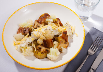 Tasty baked potatoes with garnish of cauliflower, fried bacon and mushrooms with cheese dip sauce