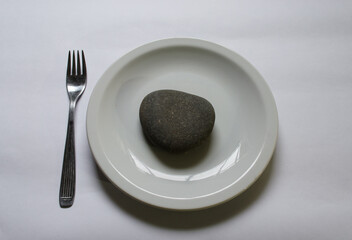White plate with a gray stone and fork on white background.