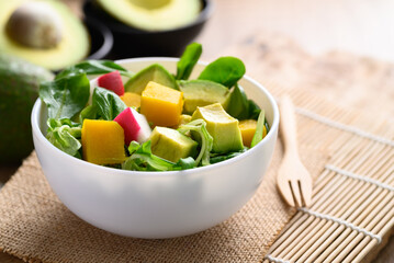 Healthy vegan salad fruits and vegetables with avocado, dragon fruit, radish, pumpkin and corn salad in a bowl on wooden