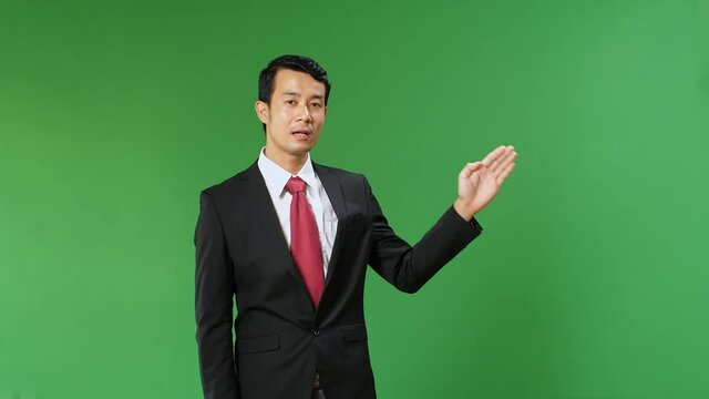 Asian Businessman Pointing On Something And Talking On A Green Screen, Chroma Key
