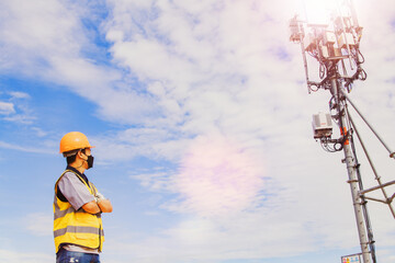 Asian male engineer wearing a mask and safety helmet plans a tower-type telecommunication antenna...