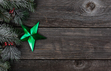 Green star ornament with snowy fir and wood background for a merry Christmas or happy New Year celebration concept