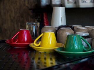 Yellow, green , and red ceramic coffee cup upside down on saucer on the metal shelf in cafe.