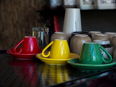 Yellow, Green , And Red Ceramic Coffee Cup Upside Down On Saucer On The Metal Shelf In Cafe.