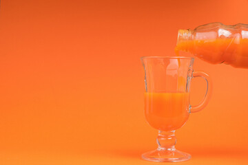 Pouring a fresh smoothie from a bottle into a glass on an orange background.