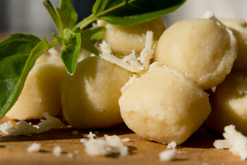 Gnocchi pasta pre-cooked on a wooden board with grated cheese and basil. Macro close up. Selective focus.