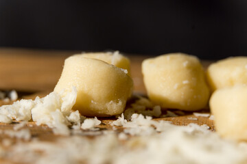 Gnocchi pasta pre-cooked on a wooden board with grated cheese and basil. Macro close up. Selective focus.