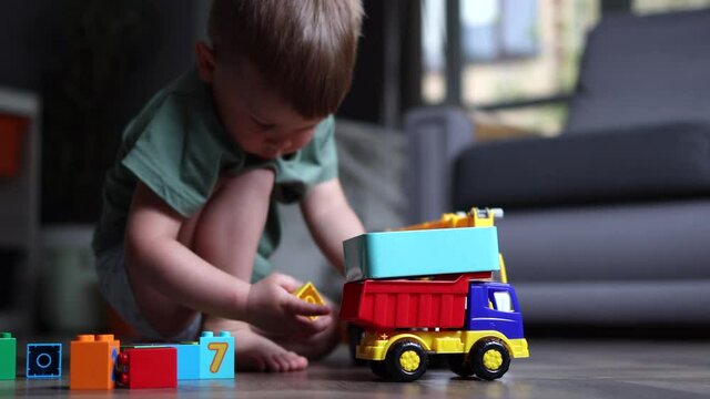 little boy child playing with toys on the wooden floor at home indoors, lifestyle concept kid education exploring