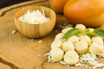 Gnocchi pasta pre-cooked on a wooden board with grated cheese, tomatoes and basil. Close up. Selective focus.