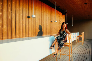 Asian woman sitting on high chair at the bar counter and watching the sunset