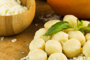 Gnocchi pasta pre-cooked on a wooden board with grated cheese, tomatoes and basil. Close up. Selective focus.