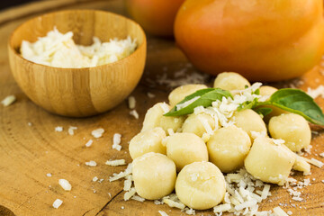 Gnocchi pasta pre-cooked on a wooden board with grated cheese, tomatoes and basil. Close up. Selective focus.