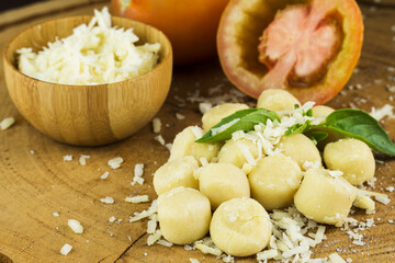 Gnocchi pasta pre-cooked on a wooden board with grated cheese, tomatoes and basil. Close up. Selective focus.