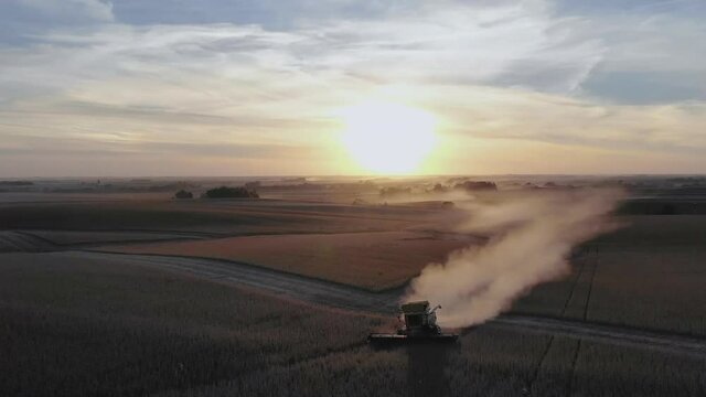 Combiner leaving large dust trail as it harvests soy beans at dusk. Aerial wide shot.