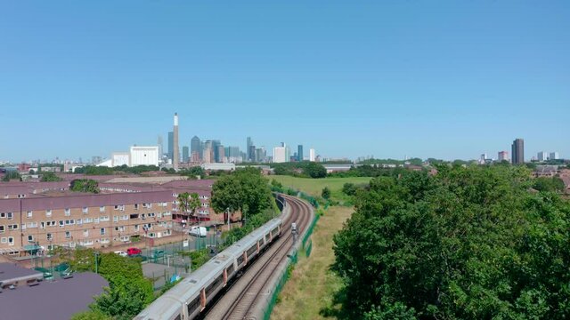 Cinematic rising drone shot of London overground train heading into the city sunny day