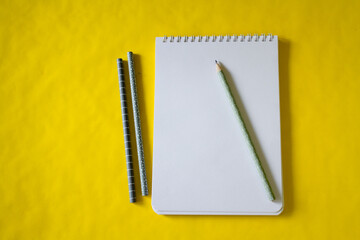 yellow background. a white notebook. pencil.