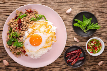 Khao Pad Ka Prao Moo Sub Kai Dao, Thai food, streamed rice with basil stir fried mince pork and fried egg beside fish sauce, basil leaves, dried chili and garlic on rustic wood background, top view