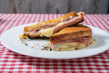 Toasted ham and cheese sandwich on a white plate on a table with a tablecloth.