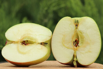Two halves of an oval-conical apple with a very tender, light green pulp on a blurred green...