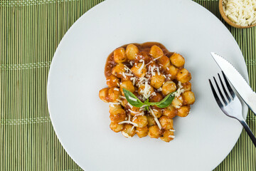 Gnocchi with juice sauce with grated cheese and basil served on the plate. Close-up. Selective focus. Top view.