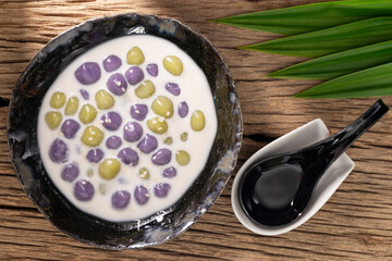 Bualoy, Bua Loy, Bualoi, Bua Loi, Thai dessert, sticky rice dumplings in sweet coconut milk, purple color from taro, green color from pandan leaf on rustic natural wood texture background, top view