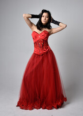 Full length  portrait of beautiful young asian woman wearing red corset and ornate gothic queen crown. Graceful standing posing  isolated on studio background.