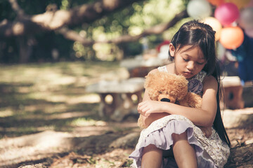 Sad girl hugging teddy bear sadness alone in green garden park. Lonely girl feeling sad unhappy sitting outdoors with best friend toy. Autism child play teddy bear best friend. Family violence concept