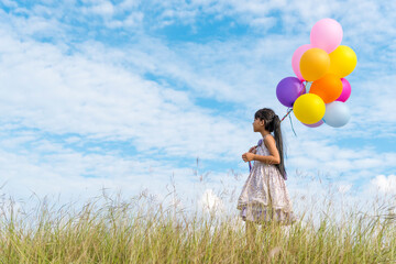 Cheerful cute girl holding balloons running on green meadow white cloud and blue sky with happiness. Hands holding vibrant air balloons play on birthday party happy times summer on sunlight outdoor