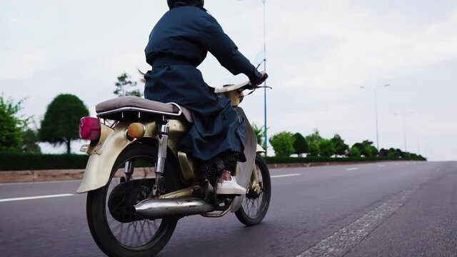Young woman rides vintage Honda Cub motorcycle on highway in Vietnam