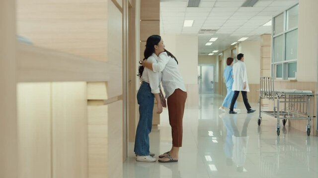 Young Asian woman embracing her mother and crying after get bad news from doctor about her father at hospital,  Women cry wait for surgical operator feel sad and hopeless in front of emergency room.