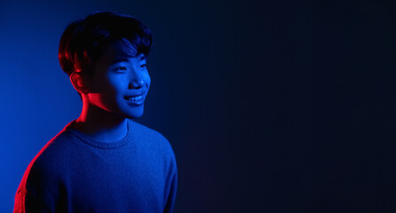 Neon light man. Cyberpunk banner. Happy smile. Positive emotion. Portrait of cheerful Asian guy in bright colorful shining red blue glow isolated on dark empty space background.
