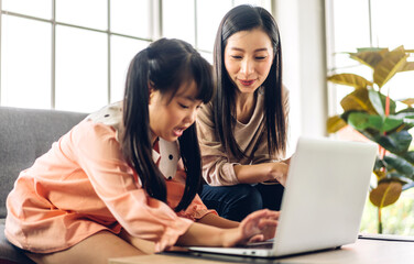 Mother and asian kid little girl learning and looking at laptop computer making homework studying knowledge with online education e-learning system.children video conference with teacher tutor at home
