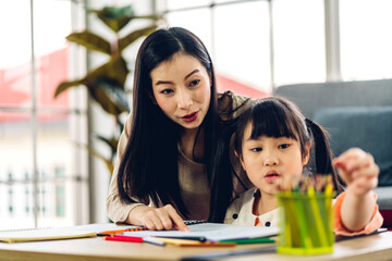 Portrait love asian family mother and little asian girl learning and writing in book with pencil making homework at home