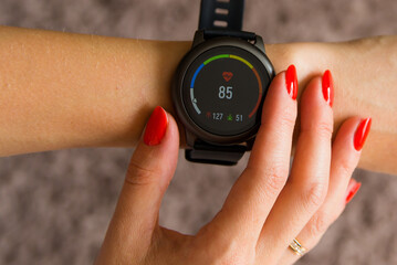 A girl with a red manicure holds a black smart watch in her hands