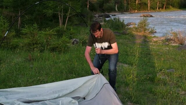 Bearded man puts up a tent on the bank of mountain river. Slow motion
