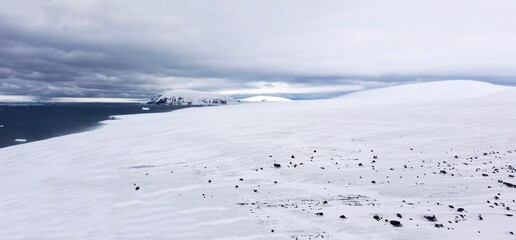 Obraz premium Panoramic view of the snowy lower slopes of Brown Bluff on the northern Antarctic peninsula. The landscape is strewn with basalt rock and the weather is cold and windy.