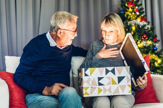 Romantic sweet senior couple having fun and smiling while celebrating enjoying opening magic christmas box.Senior man giving gift box surprise to wife in valentines day at home - Powered by Adobe
