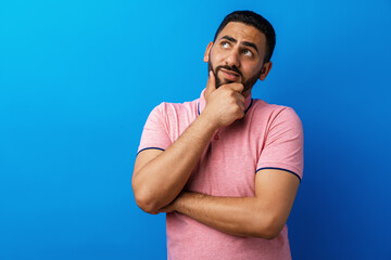 Pensive young arab man thinking and looking up against blue background